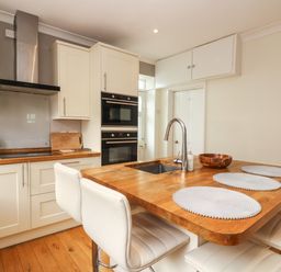 A kitchen with wooden countertops white cabinets an island with a sink four white chairs and built in ovens at Pound Rocks in Tintagel