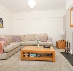 A living room with a beige sectional sofa a wooden coffee table with books and wine glasses a fireplace and a lamp on wooden nesting tables at Pound Rocks in Tintagel