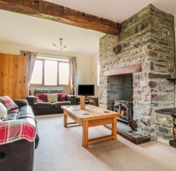 A living room with two sofas a wooden coffee table and a stone fireplace with firewood at Blaen Henllan in Builth Wells