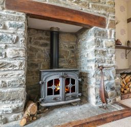 A stone fireplace with a wood burning stove and stacked firewood at Blaen Henllan in Builth Wells