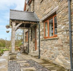 Stone exterior wall of a house with wooden framed windows a covered porch with wooden posts and outdoor seating at Blaen Henllan in Builth Wells