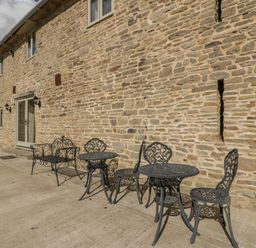 A stone wall with metal tables and chairs outside a building at Timber Barn in Eardisland