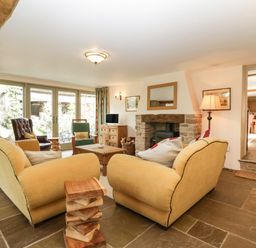 A living room with two yellow sofas a wooden coffee table a fireplace and glass doors at Timber Barn in Eardisland