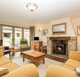 A living room with yellow sofas a stone fireplace a wooden coffee table and large glass doors at Timber Barn in Eardisland