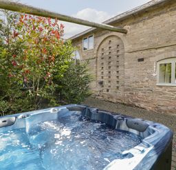 An outdoor hot tub with bubbling water near a stone building and trees at Timber Barn in Eardisland