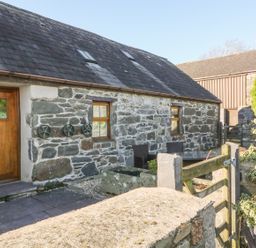 A stone building with a wooden door and windows with outdoor seating behind a wooden gate at Beudy Bach in Y Felinheli