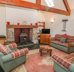 A living room with three plaid sofas around a wooden coffee table a stone fireplace exposed wooden beams and a television on a cabinet at Beudy Bach in Y Felinheli