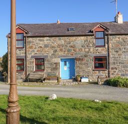 A stone house with a blue door and red window frames next to a gravel path and green grass at Hendre in Y Felinheli