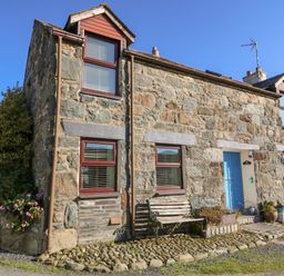 A stone cottage with a blue door a bench and potted plants outside at Hendre in Y Felinheli