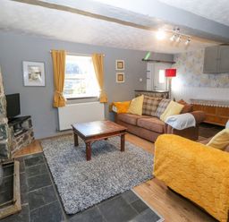 A living room with two brown sofas yellow cushions and throws a wooden coffee table stone fireplace and a window with yellow curtains at Hendre in Y Felinheli