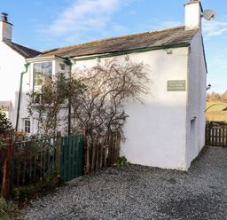 Exterior view of a white house with two chimneys a green gate gravel driveway and surrounding vegetation at Castle Lodge in Borrowdale