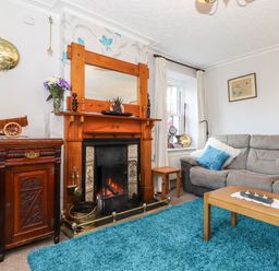A living room with a fireplace wooden furniture blue rug and gray sofa at Castle Lodge in Borrowdale