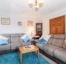 A living room with two gray sofas, a wooden coffee table, a blue rug, framed pictures on the wall, and a wooden cabinet at Castle Lodge in Borrowdale