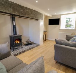 A living room with a wood burning stove between two sofas a wall mounted television a window and wooden flooring at Y Cilgwyn in Trawsfynydd