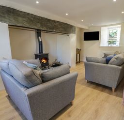 A living room with two grey sofas a wood burning stove a wall mounted television and a window at Y Cilgwyn in Trawsfynydd