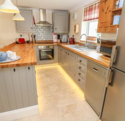 A kitchen with wooden countertops gray cabinets a sink oven dishwasher and stainless steel refrigerator at Pottery Cottage in Begelly near Kilgetty
