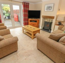 A living room with sofas a coffee table a television wood stove and glass doors at Pottery Cottage in Begelly near Kilgetty