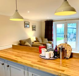 A kitchen island with cups and a teapot with a living area featuring armchairs and a lamp beside glass doors at Pottery Cottage in Begelly near Kilgetty