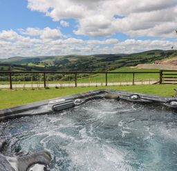 An outdoor hot tub with bubbles overlooking green hills and a partly cloudy sky at Shepherd's View in Rhayader