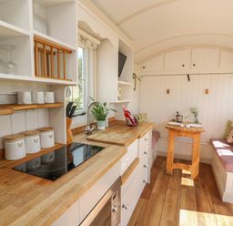 A kitchen space with wooden countertops white cabinets a small dining table and bench seating at Shepherd's View in Rhayader