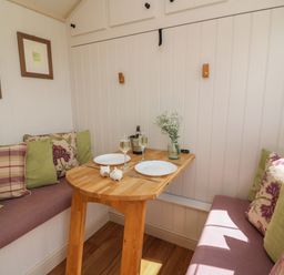 A small dining nook with wooden table set with two plates glasses and decorations at Shepherd's View in Rhayader
