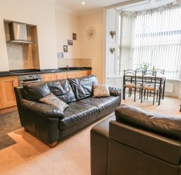 An open plan living room and kitchen with a black leather sofa and armchair a dining table with four chairs and a television at Flat 4 in Whitby