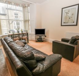 A living room with black leather sofa armchair dining table and television at Flat 4 in Whitby