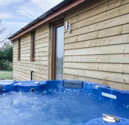 An outdoor hot tub next to a wooden building with glass door and small windows at Gardener's Lodge in Nantwich