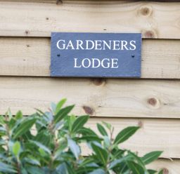 A wooden wall with a sign that reads Gardeners Lodge and some green leaves in front at Gardeners Lodge in Nantwich