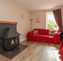A living room with a fireplace and red sofa at The Farmhouse in Brynsiencyn near Newborough