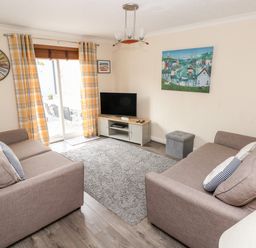A living room with two sofas a television on a stand and a large wall clock at Sandy Bay House in Saundersfoot