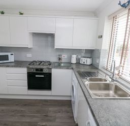 A kitchen with white cabinets microwave oven kettle toaster and stainless steel sink at Sandy Bay House in Saundersfoot