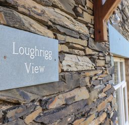 A stone wall with a sign reading Loughrigg View and a window at Loughrigg View in Ambleside