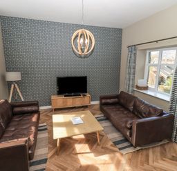 A living room with two brown leather sofas a wooden coffee table and a TV on a wooden stand at Loughrigg View in Ambleside