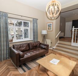 A living room with a brown leather sofa a wooden coffee table and a window with striped curtains at Loughrigg View in Ambleside