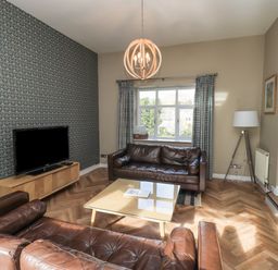 A living room with brown leather sofas a glass coffee table a wooden TV stand with a television and patterned wallpaper at Loughrigg View in Ambleside