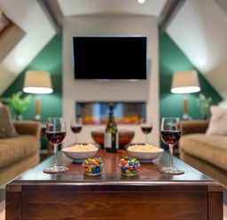 A living room with two sofas a wooden coffee table with wine glasses bowls of popcorn and jars of colorful candies a wall-mounted television and two lamps at Geltsdale East Wing in Wetheral