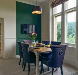 A dining room with a wooden table set for breakfast and blue chairs at Geltsdale East Wing in Wetheral