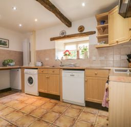 A kitchen with wooden cabinets a washing machine dishwasher and a window with plants and plates on the wall at Springarth Cottage in Newby