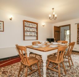A dining room with a wooden table set for six and a wooden plate rack on the wall at Springarth Cottage in Newby