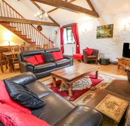 A living room with leather sofas wooden coffee table red and black cushions and wooden staircase at The Old Byre in Appleby-in-Westmorland