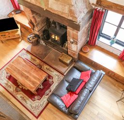 A living room with a leather sofa red cushions wooden coffee table fireplace and television at The Old Byre in Appleby-in-Westmorland