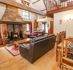 A living room with a stone fireplace leather sofas and a wooden dining table at The Old Byre in Appleby-in-Westmorland