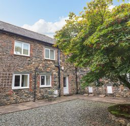 A stone courtyard with a tree in a raised stone planter and patio furniture at Maple Cottage in Keswick