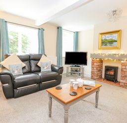 A living room with a black leather sofa a wooden coffee table and a TV by a brick fireplace at Maple Cottage in Keswick