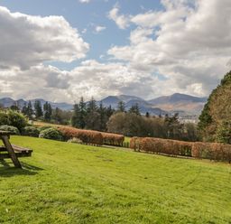 A grassy garden with a wooden picnic bench and hedges overlooking distant hills and trees at Garden Cottage in Keswick