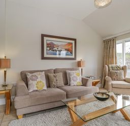 A living room with a sofa, armchair, glass coffee table, side tables, and a framed picture at Garden Cottage in Keswick
