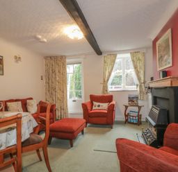 A living room with red armchairs and ottoman near a fireplace with paintings on walls at Derwent Edge in Portinscale