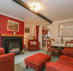 A living room with red armchairs a fireplace a dining table and kitchen in the background at Derwent Edge in Portinscale