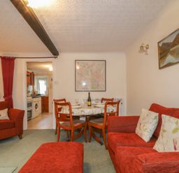 A sitting room with red chairs a dining table and a view into the kitchen at Derwent Edge in Portinscale